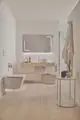 Badezimmer mit hellen Holz- und weißen Elementen. Zu sehen sind ein moderner Waschtisch und eine Ideal Standard-Waschtischarmatur, sowie dekorative Accessoires und Handtücher.